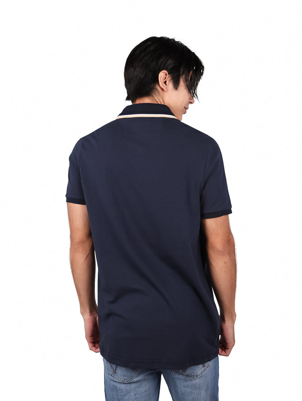 Hombre vistiendo una playera polo de color marino con detalle en el cuello y pantalones mezclilla azules.