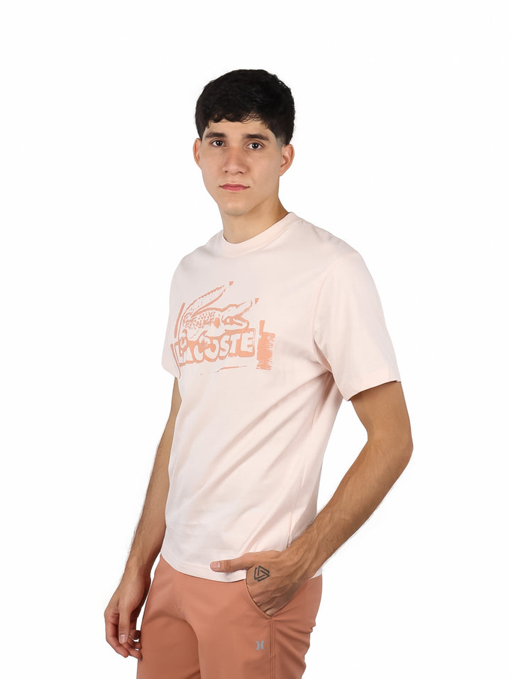 Hombre vistiendo camiseta de manga corta color rosa pálido con gráfico estampado en el frente.
