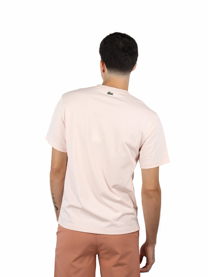 Hombre vistiendo camiseta de manga corta color rosa pálido con gráfico estampado en el frente.
