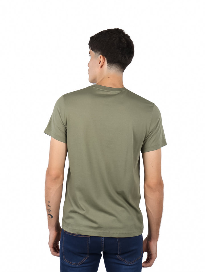 Hombre vistiendo camiseta de manga corta color kaki con gráfico de cocodrilo y texto Lacoste en el pecho.