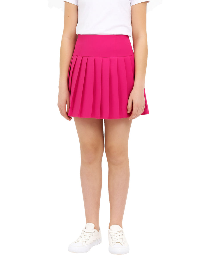 Niña vistiendo una falda corta de color fucsia con diseño de medio tablón y tenis blancos.