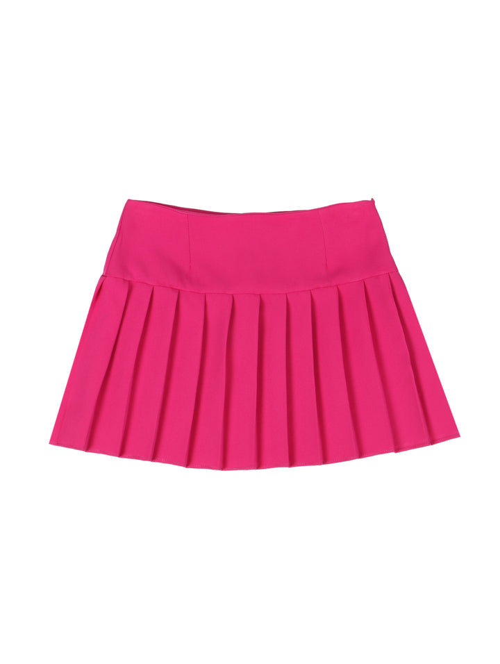 Niña vistiendo una falda corta de color fucsia con diseño de medio tablón y tenis blancos.