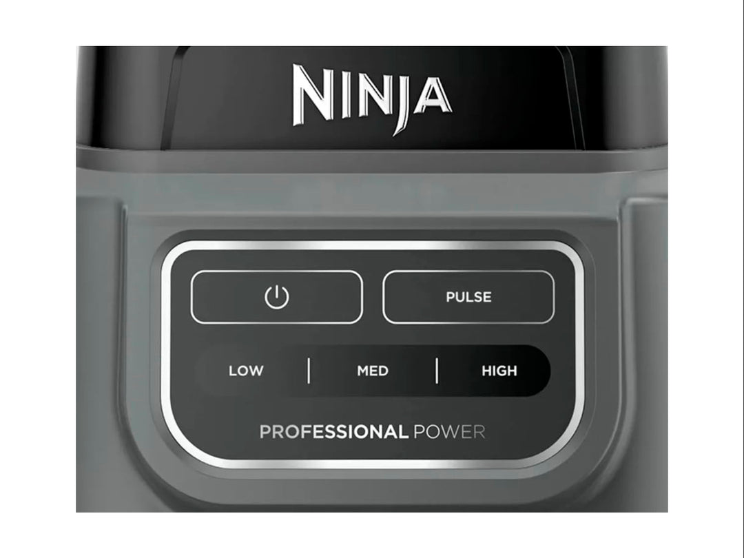 Licuadora Ninja Professional en color negro y gris con vaso de plástico transparente lleno de frutas verdes.