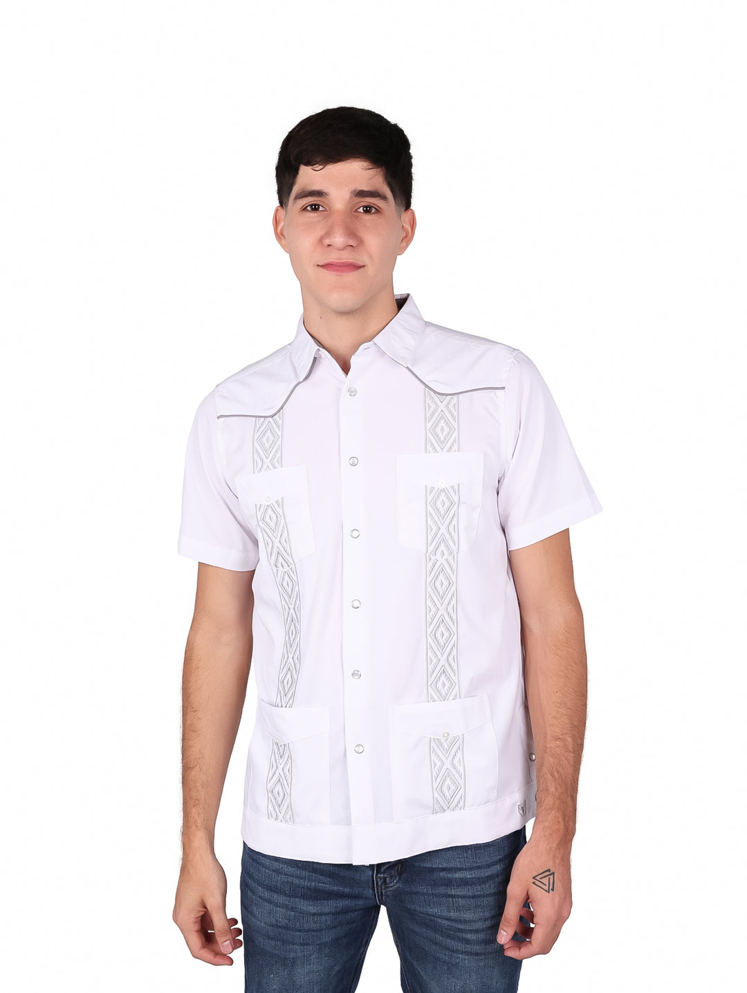 Hombre vistiendo una guayabera blanca de manga corta con detalles bordados en gris y pantalones jeans azules.