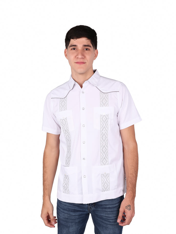 Hombre vistiendo una guayabera blanca de manga corta con detalles bordados en gris y pantalones jeans azules.