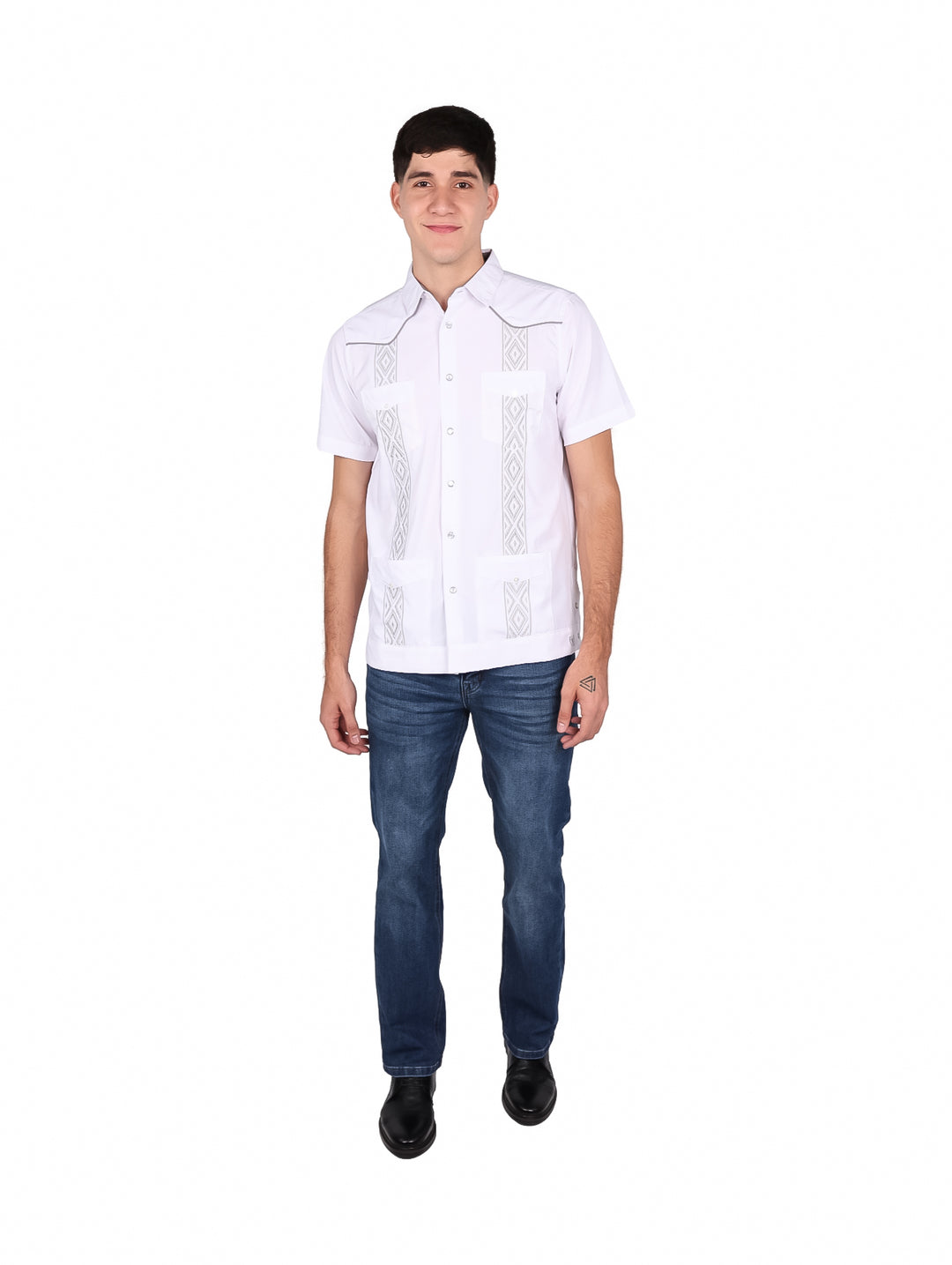 Hombre vistiendo una guayabera blanca de manga corta con detalles bordados en gris y pantalones jeans azules.