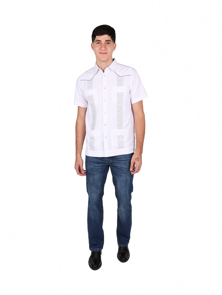 Hombre vistiendo una guayabera blanca de manga corta con detalles bordados en gris y pantalones jeans azules.