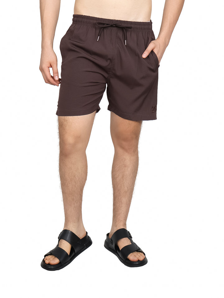 Hombre vistiendo un traje de baño tipo short color café con cordón ajustable y bolsillos laterales.