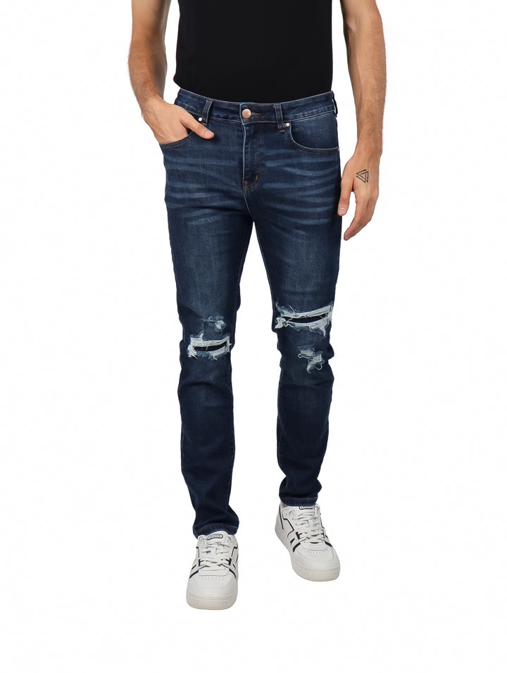 Hombre vistiendo jeans slim fit color azul oscuro con detalles rotos en las rodillas.