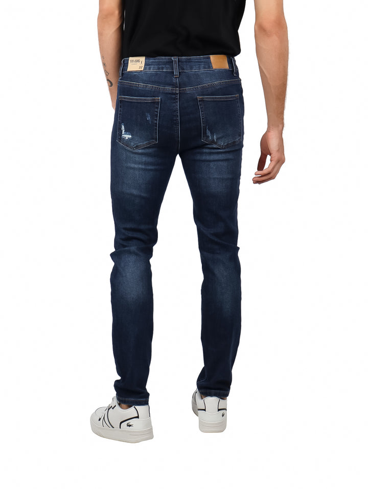 Hombre vistiendo jeans slim fit color azul oscuro con detalles rotos en las rodillas.