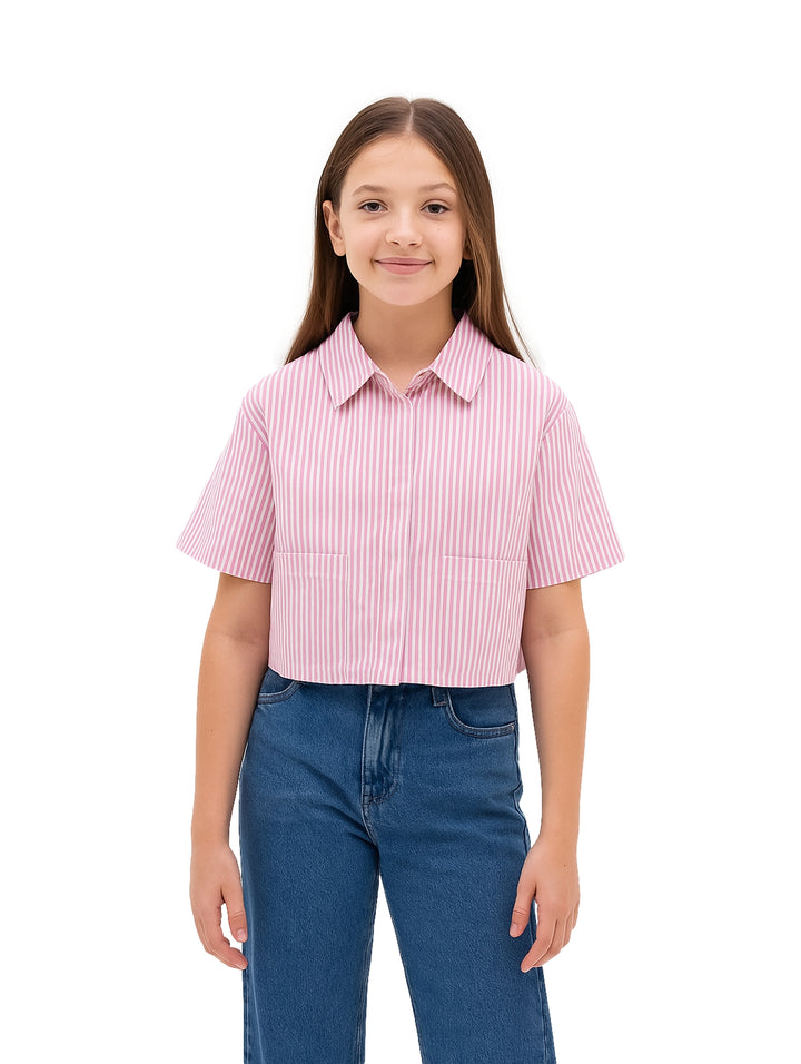 Niña vistiendo una camisa rosa con rayas blancas verticales, manga corta y cuello, combinada con pantalones azules.