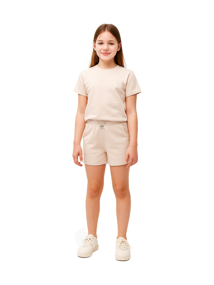 Niña vistiendo un conjunto de camiseta y shorts en color beige con tenis a juego.