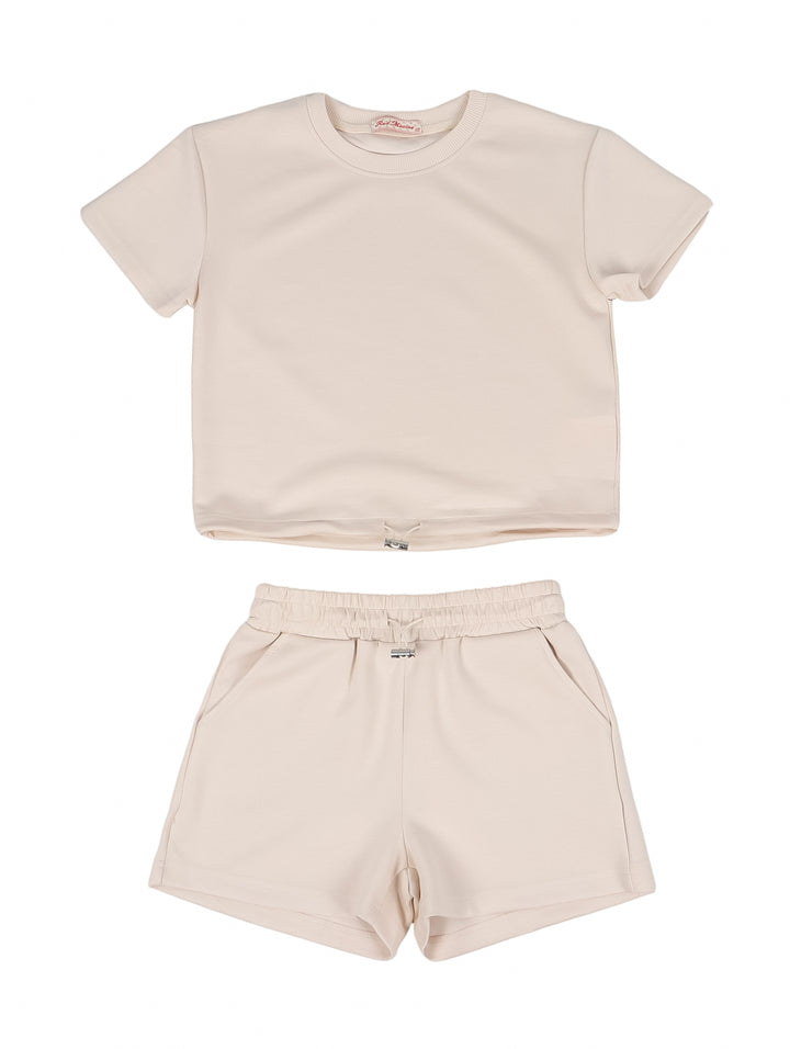 Niña vistiendo un conjunto de camiseta y shorts en color beige con tenis a juego.