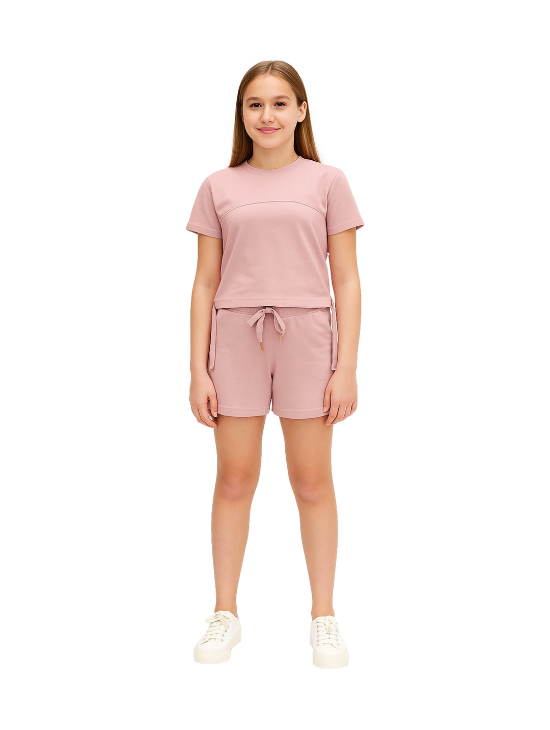 Niña vistiendo un conjunto de camiseta y shorts en color rosa con tenis blancos.