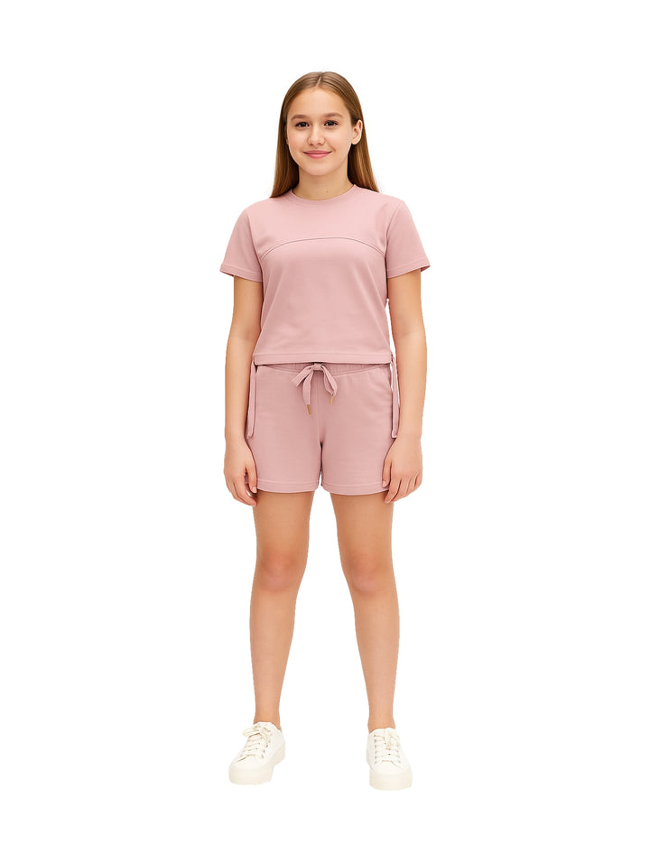 Niña vistiendo un conjunto de camiseta y shorts en color rosa con tenis blancos.