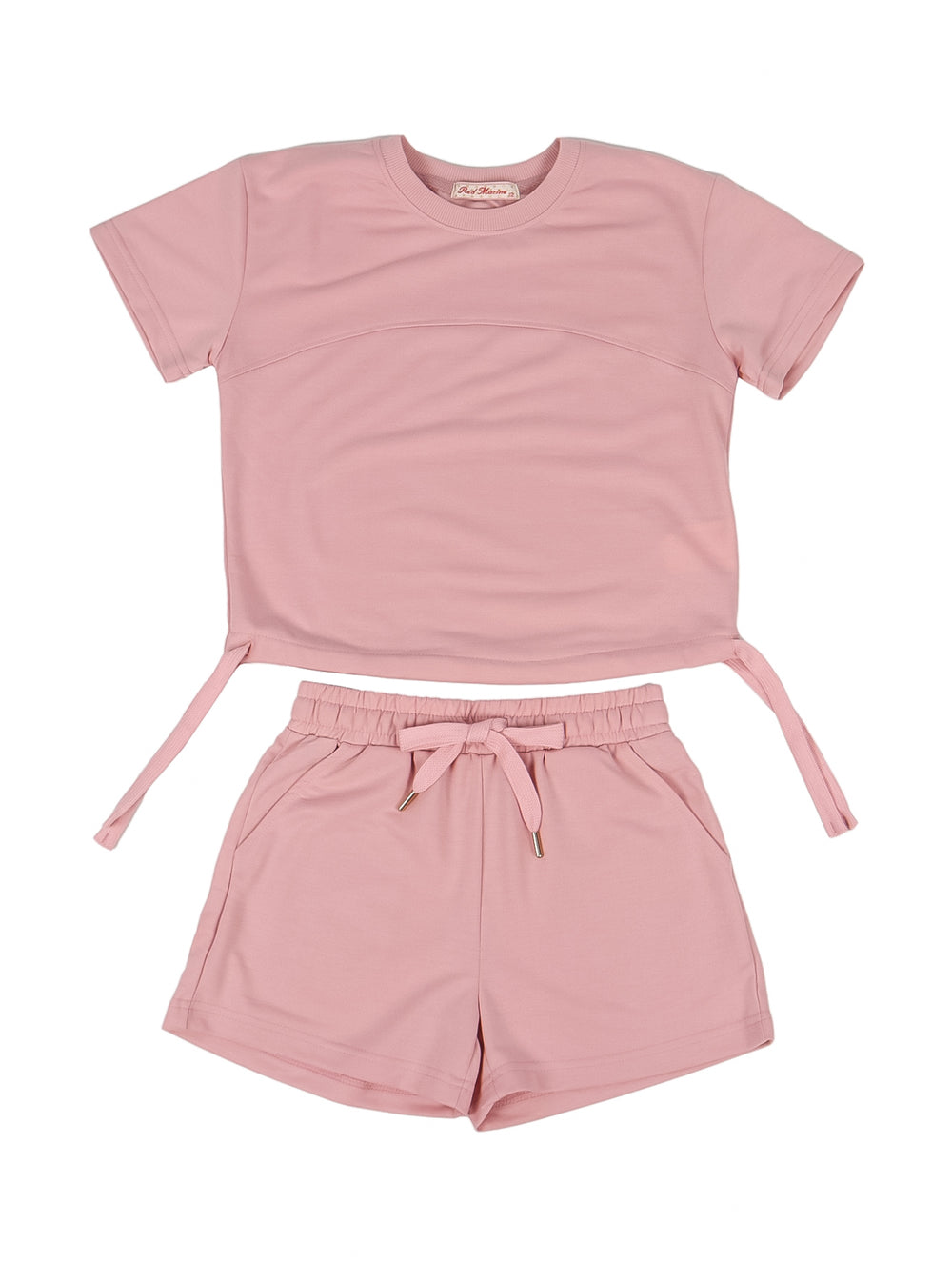 Niña vistiendo un conjunto de camiseta y shorts en color rosa con tenis blancos.
