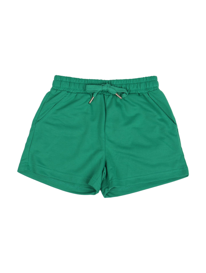 Niña vistiendo un conjunto de camiseta y short color verde con tenis blancos.