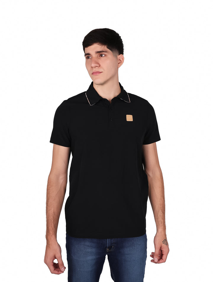 Hombre vistiendo una playera tipo polo de color negro con un pequeño detalle marrón en el pecho.