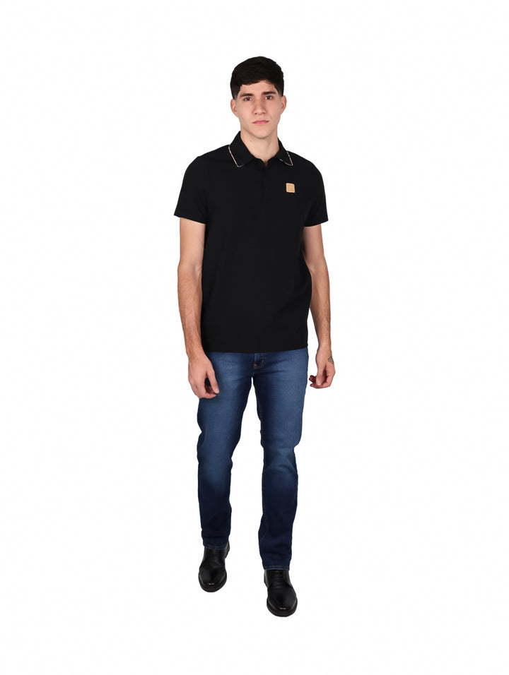 Hombre vistiendo una playera tipo polo de color negro con un pequeño detalle marrón en el pecho.