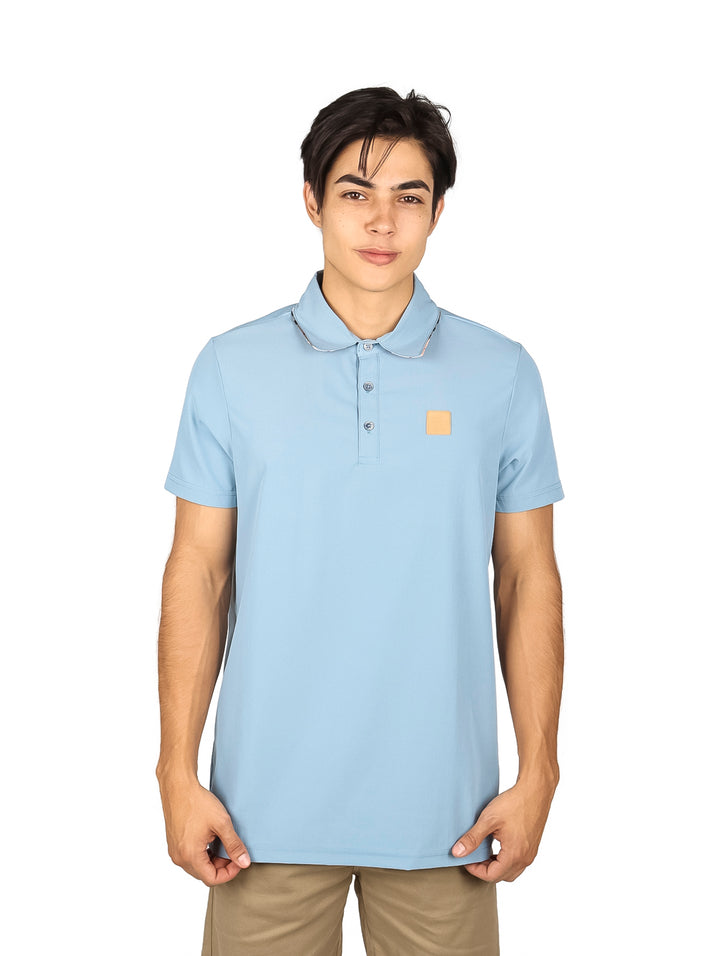 Hombre vistiendo una playera polo de color azul cielo con un pequeño parche marrón en el pecho.