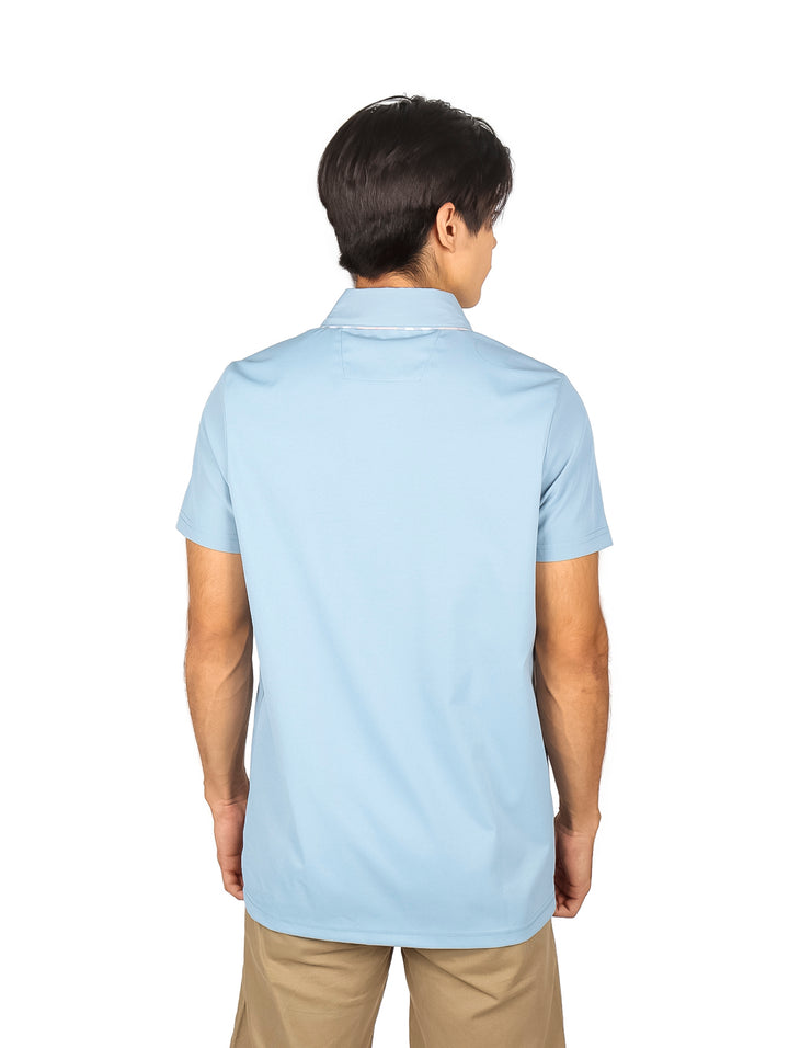 Hombre vistiendo una playera polo de color azul cielo con un pequeño parche marrón en el pecho.