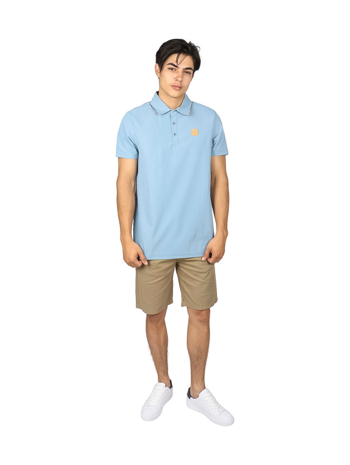 Hombre vistiendo una playera polo de color azul cielo con un pequeño parche marrón en el pecho.