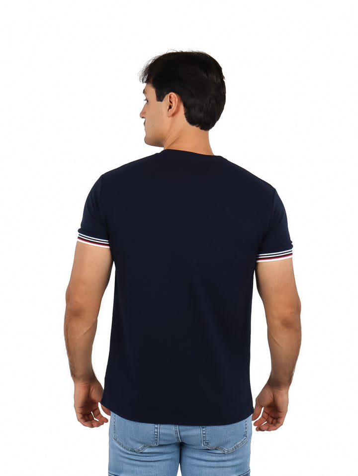 Hombre vistiendo playera azul marino de manga corta con detalles de rayas blancas y rojas en los bordes de las mangas.