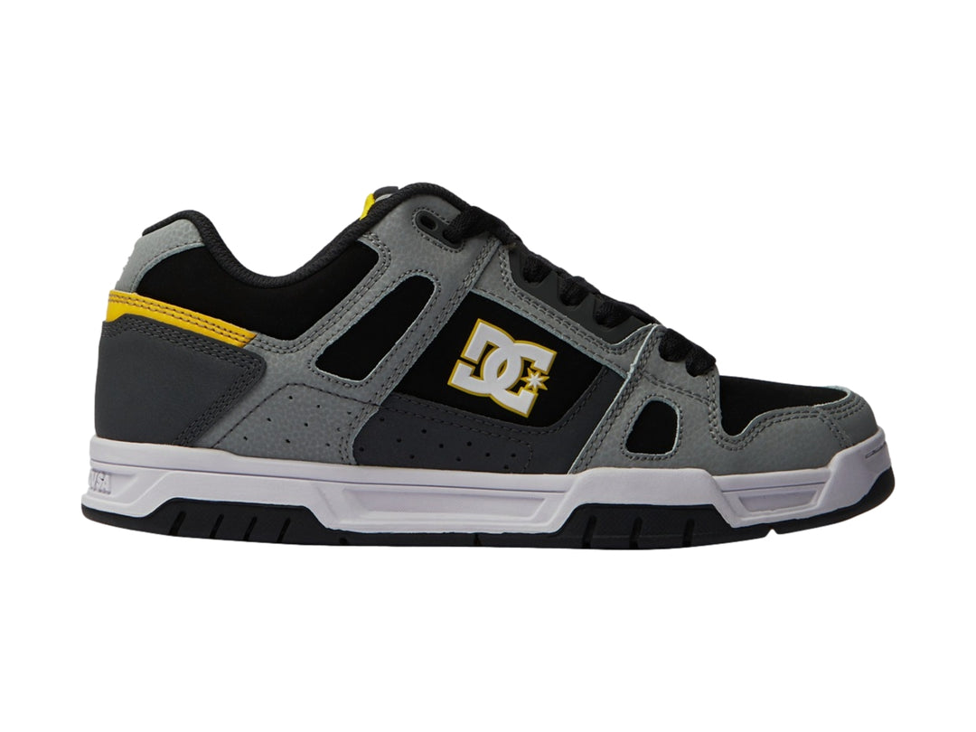Tenis DC Shoes color gris y negro con detalles amarillos y suela blanca.