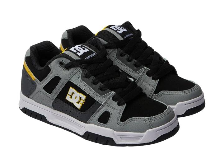 Tenis DC Shoes color gris y negro con detalles amarillos y suela blanca.