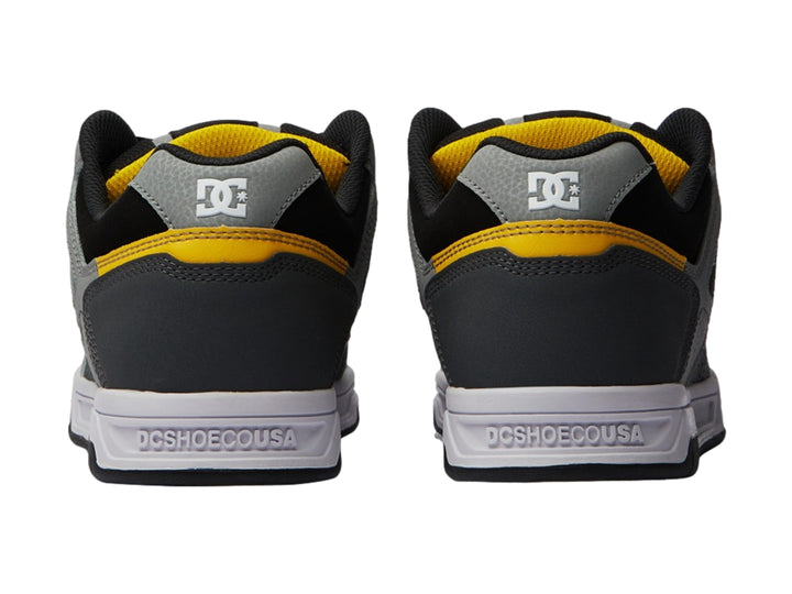 Tenis DC Shoes color gris y negro con detalles amarillos y suela blanca.