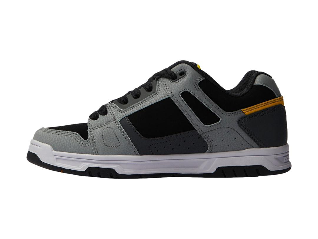 Tenis DC Shoes color gris y negro con detalles amarillos y suela blanca.