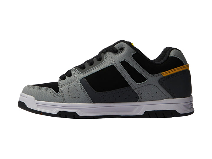 Tenis DC Shoes color gris y negro con detalles amarillos y suela blanca.
