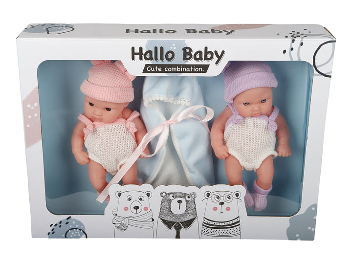 Set de dos muñecos bebés con ropa tejida en colores rosa y morado, acompañados de una manta azul en su empaque.