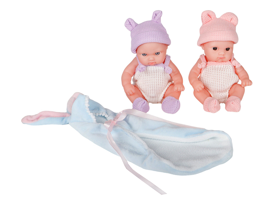 Set de dos muñecos bebés con ropa tejida en colores rosa y morado, acompañados de una manta azul en su empaque.