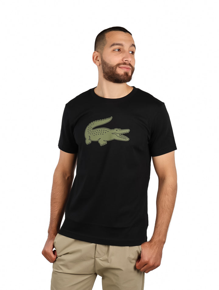 Hombre vistiendo camiseta negra de manga corta con un logotipo grande de cocodrilo en color kaki en el pecho.