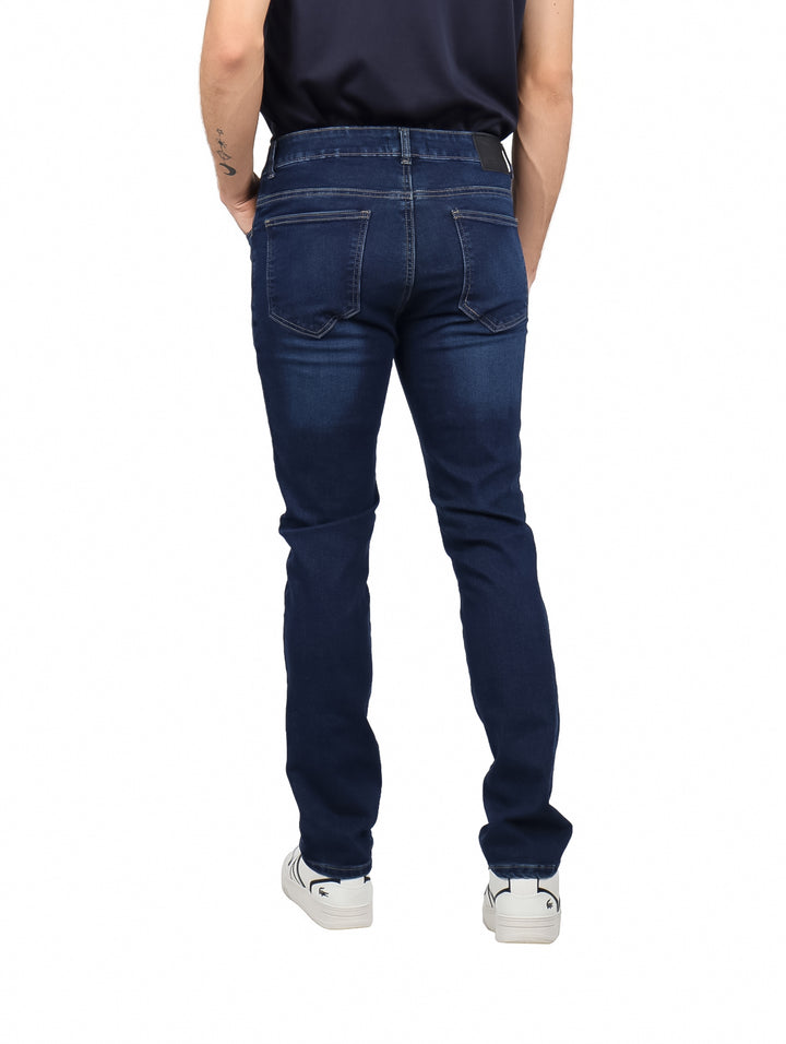 Hombre vistiendo pantalones de mezclilla color azul índigo y tenis blancos.