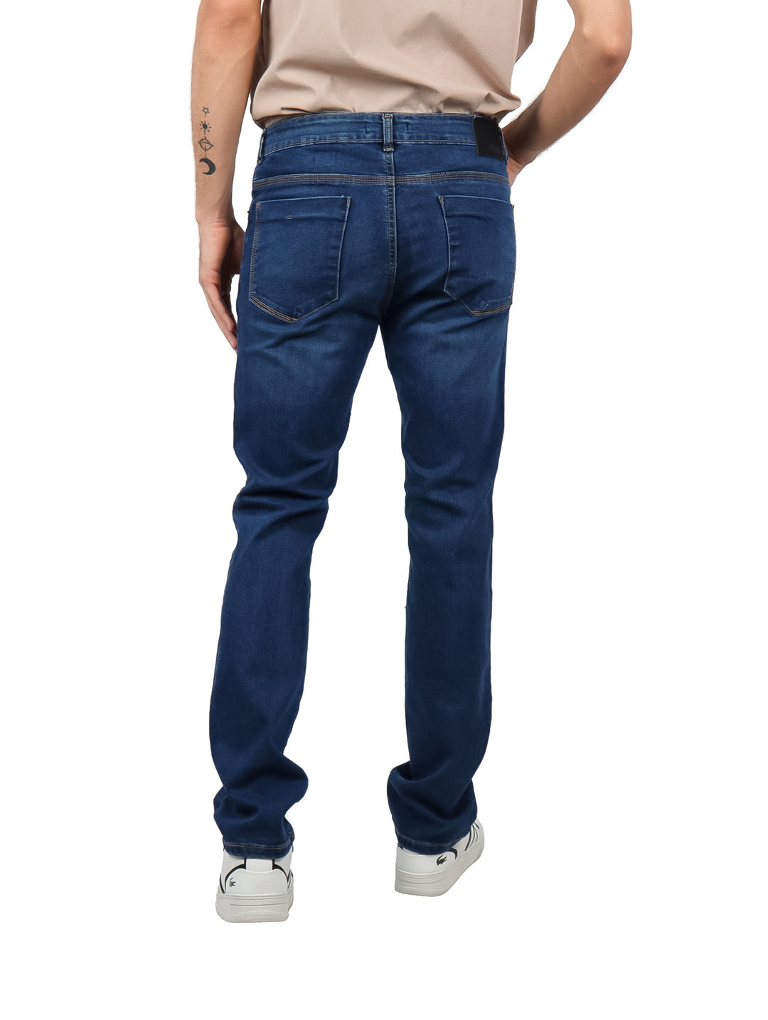 Hombre vistiendo pantalones jeans azul oscuro y tenis blancos sobre fondo blanco.