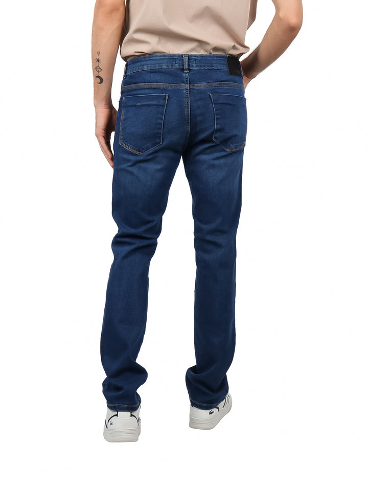 Hombre vistiendo pantalones jeans azul oscuro y tenis blancos sobre fondo blanco.