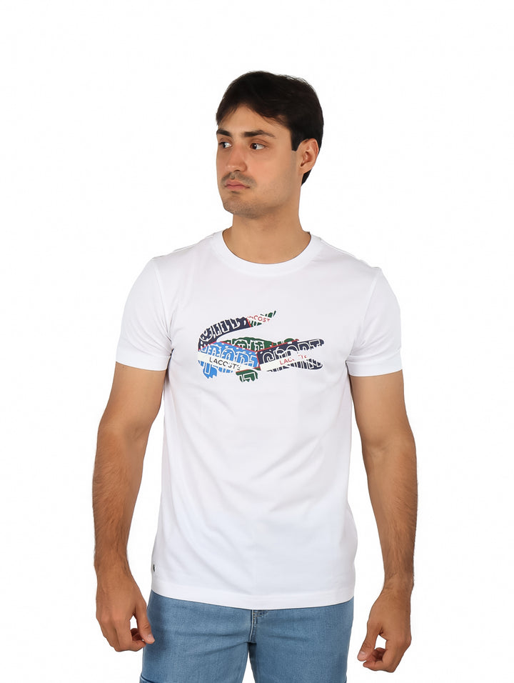 Hombre vistiendo una camiseta blanca de manga corta con un logotipo colorido de cocodrilo en el pecho.