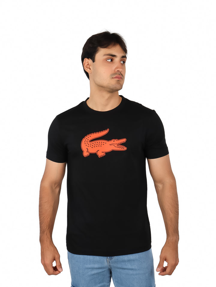 Hombre vistiendo una camiseta negra de manga corta con un logotipo grande de cocodrilo naranja en el pecho.