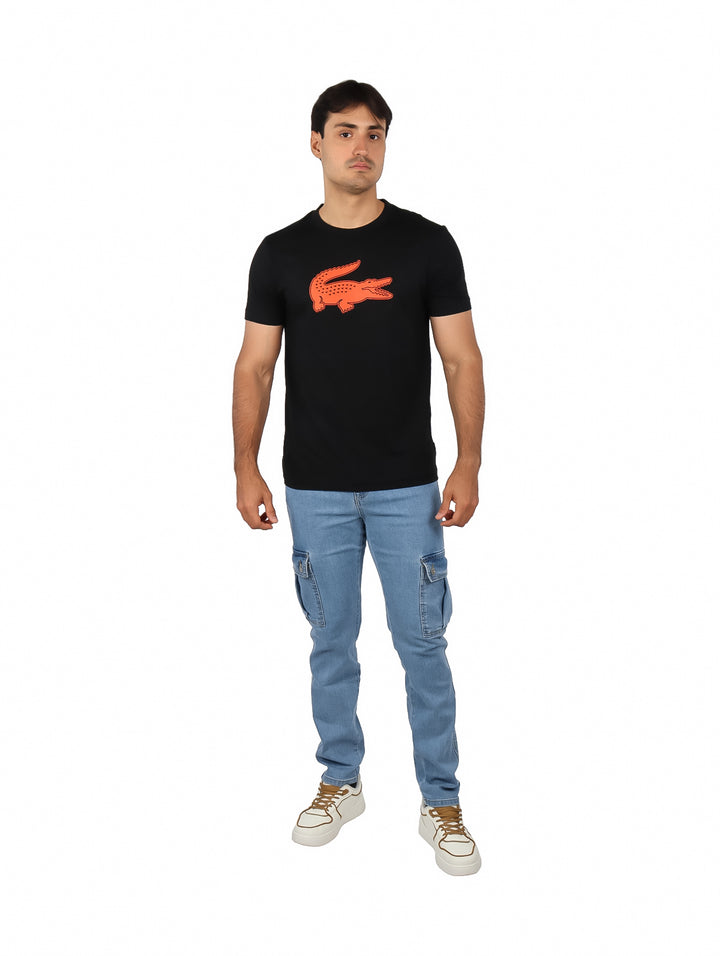 Hombre vistiendo una camiseta negra de manga corta con un logotipo grande de cocodrilo naranja en el pecho.