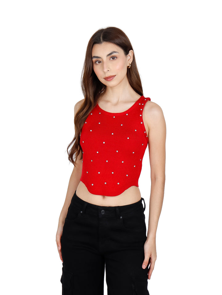 Mujer vistiendo un crop top rojo sin mangas con pequeños detalles brillantes y pantalones negros.