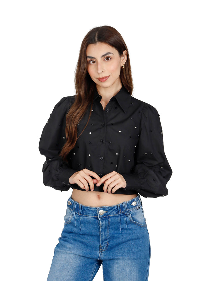 Mujer vistiendo una camisa crop top negra con detalles de perlas y jeans azules.