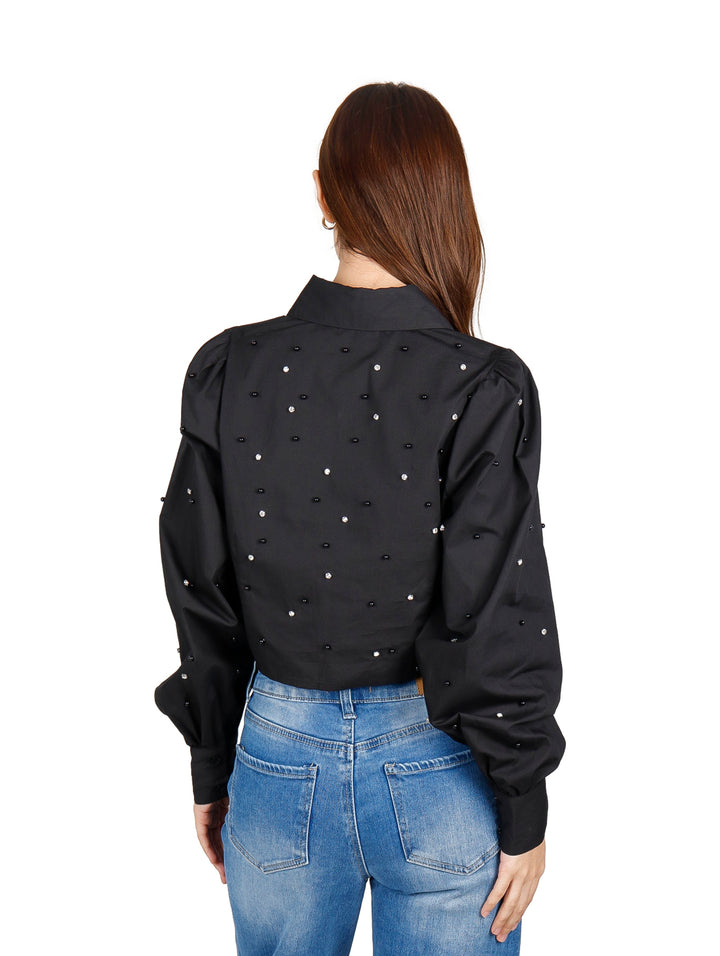Mujer vistiendo una camisa crop top negra con detalles de perlas y jeans azules.