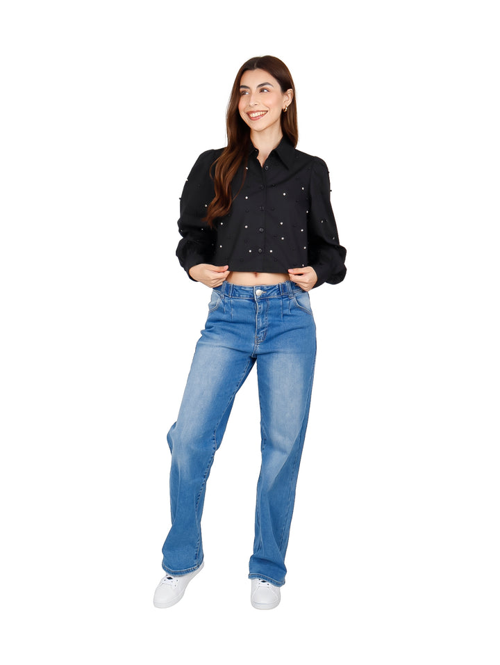Mujer vistiendo una camisa crop top negra con detalles de perlas y jeans azules.