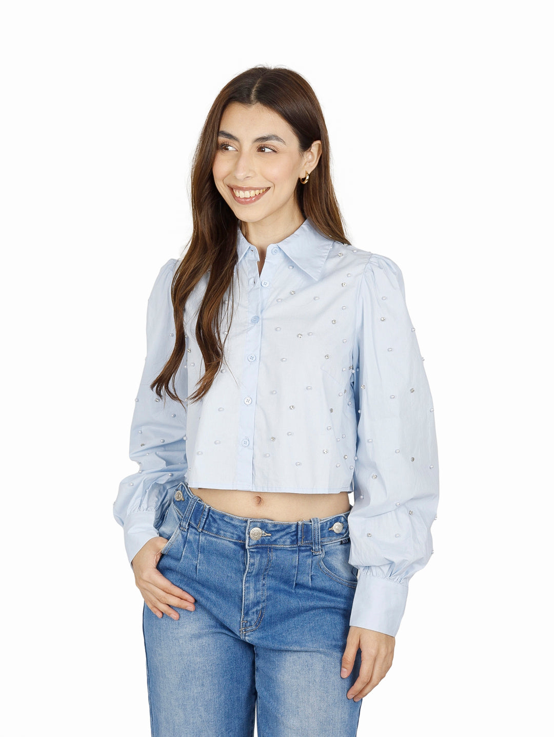 Mujer vistiendo camisa cropped azul claro con detalles de perlas y jeans azules.