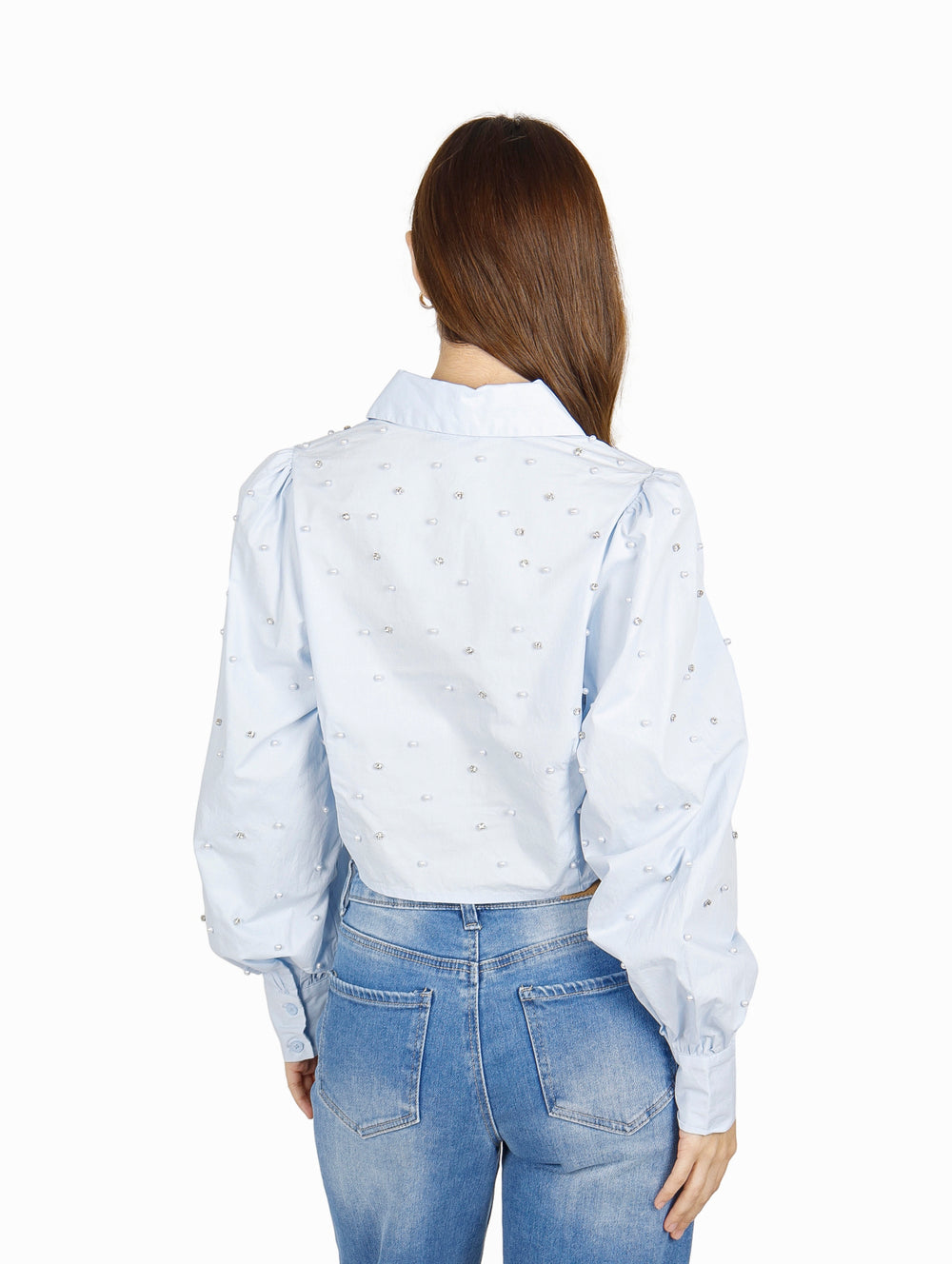 Mujer vistiendo camisa cropped azul claro con detalles de perlas y jeans azules.