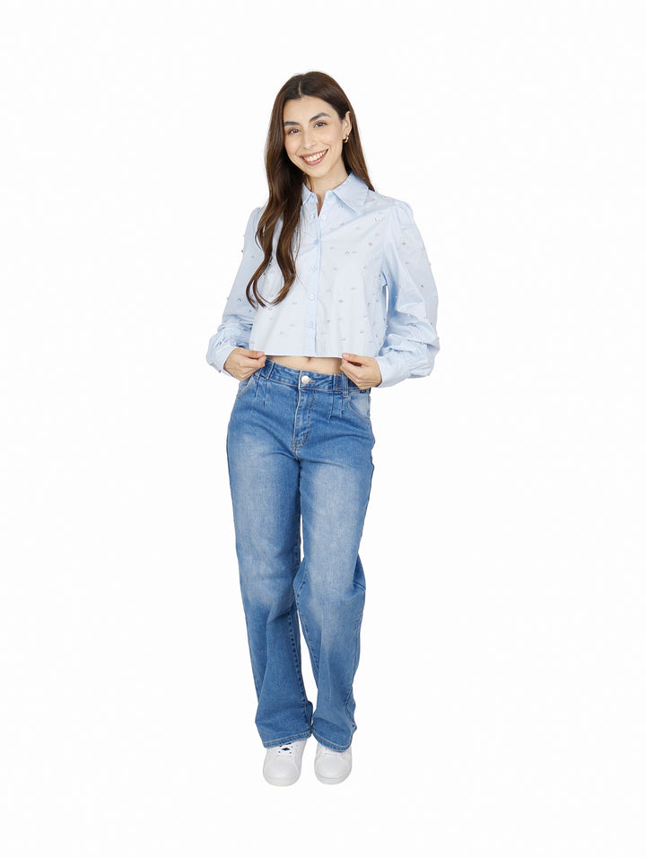 Mujer vistiendo camisa cropped azul claro con detalles de perlas y jeans azules.