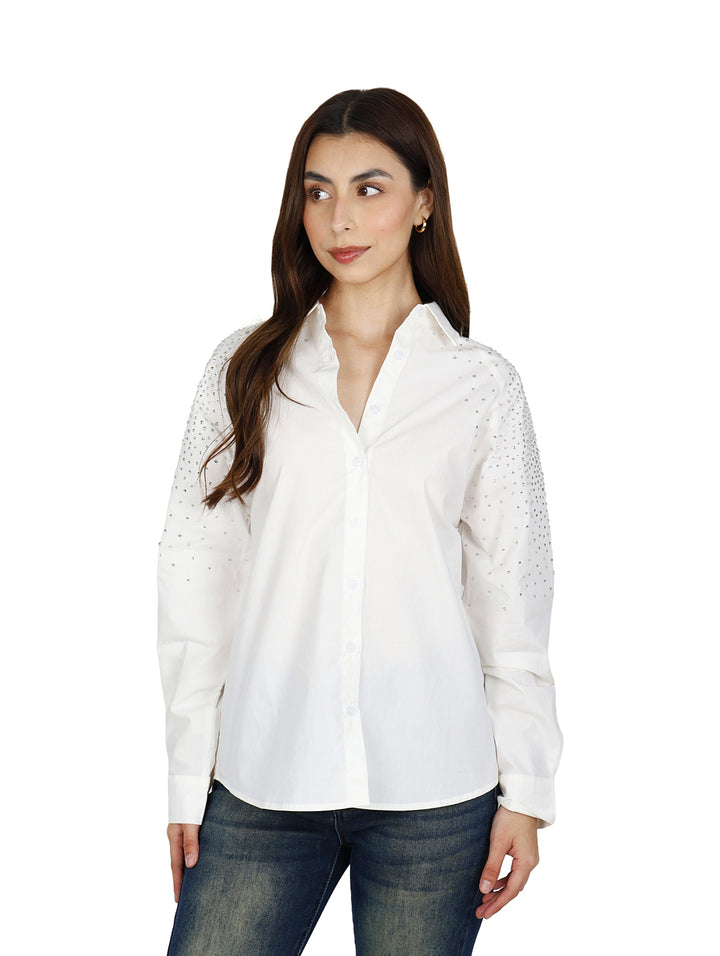 Mujer vistiendo una camisa blanca oversize de manga larga con detalles brillantes en los hombros.