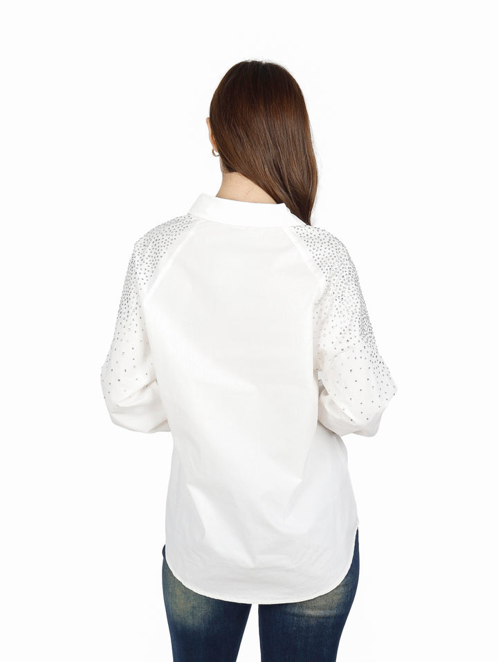 Mujer vistiendo una camisa blanca oversize de manga larga con detalles brillantes en los hombros.